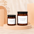 Two amber glass candles with black lids, featuring text about holding a bouquet and composure.
