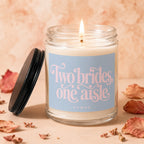 Burning glass jar candle with a light blue label that reads "Two brides, one aisle."