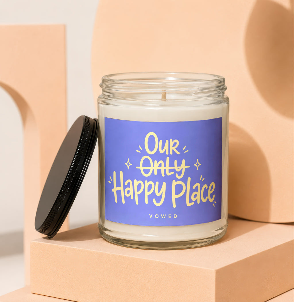 Glass candle with black lid, featuring a purple label with yellow text "Our Only Happy Place VOwed".