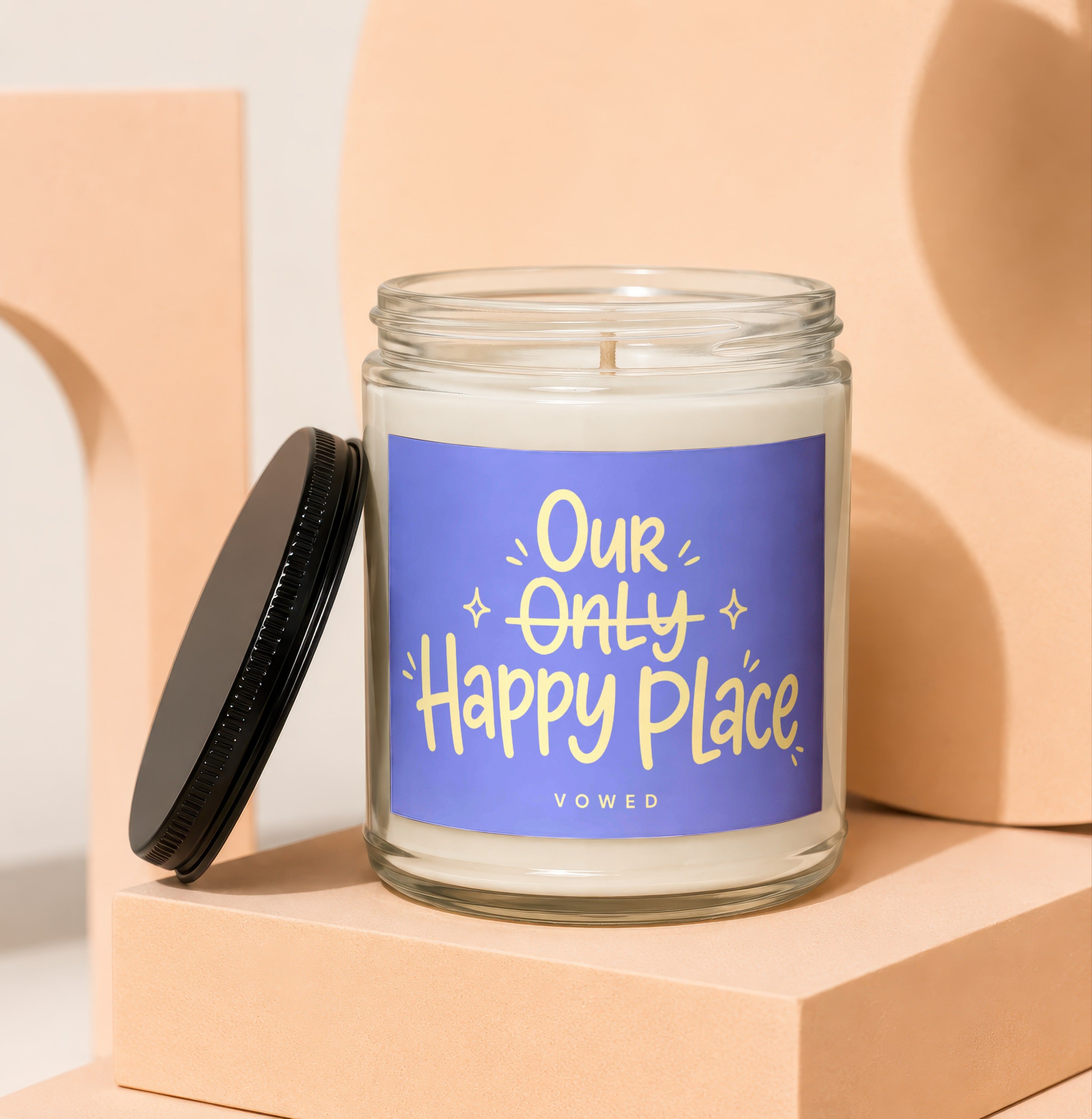 Glass candle with black lid, featuring a purple label with yellow text "Our Only Happy Place VOwed".