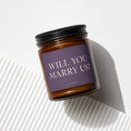 Amber glass candle with "WILL YOU MARRY US?" text on purple label.