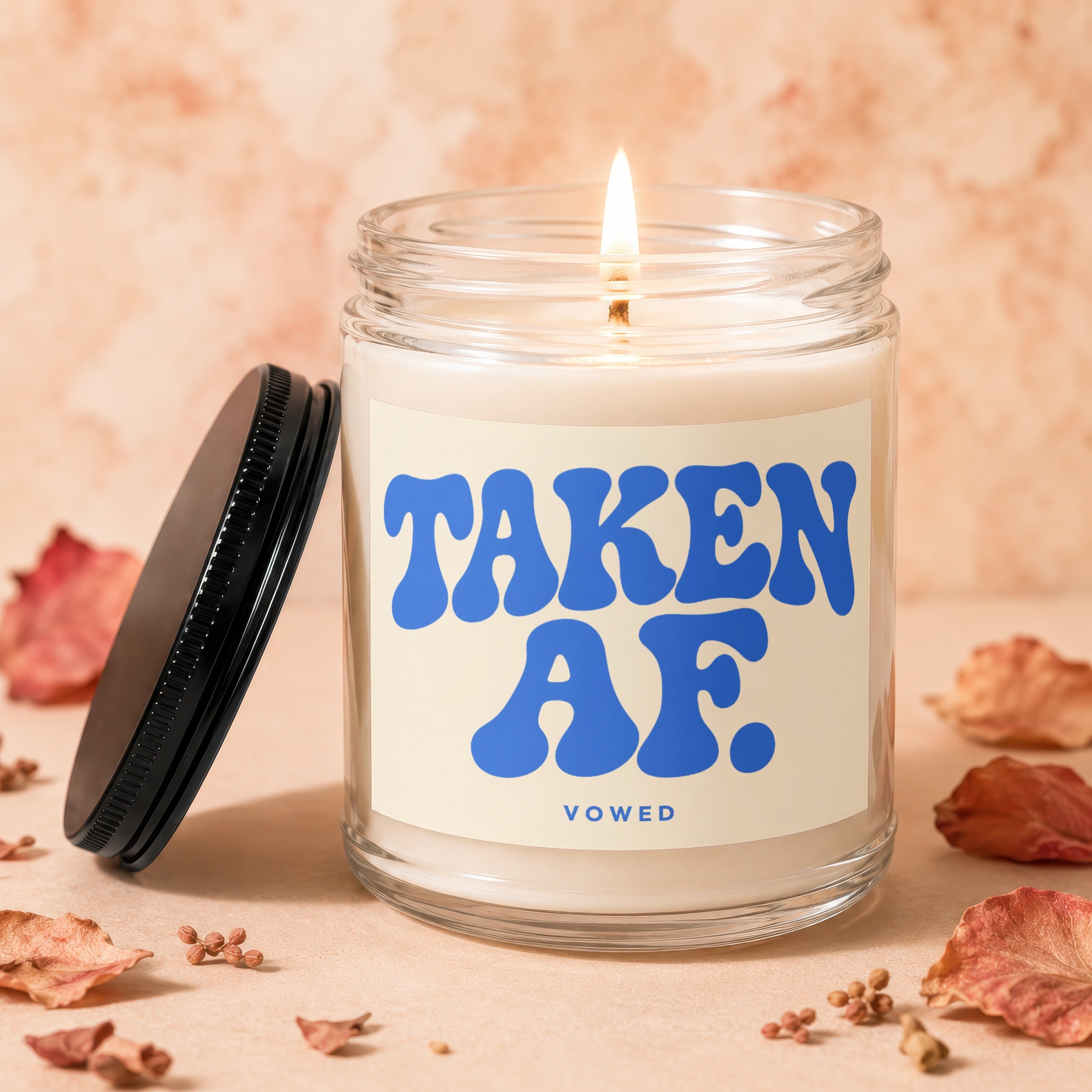 Glass candle with lit wick labeled "TAKEN AF. VOWED".