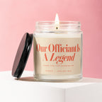 Glass jar candle reading "Our Officiant Is A Legend" with a lit wick.