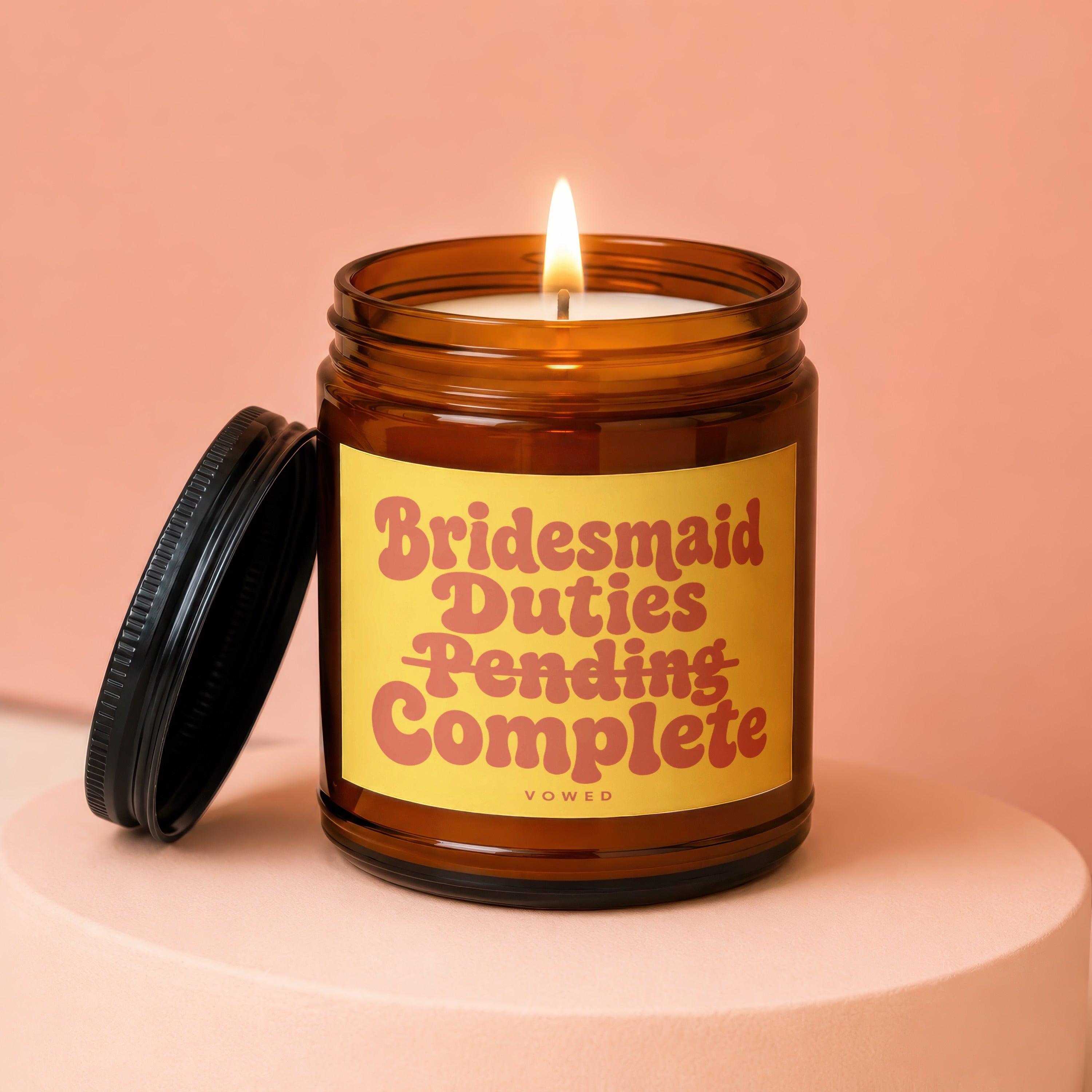 Amber jar candle with lit flame and lid nearby, labeled "Bridesmaid Duties Pending Complete".