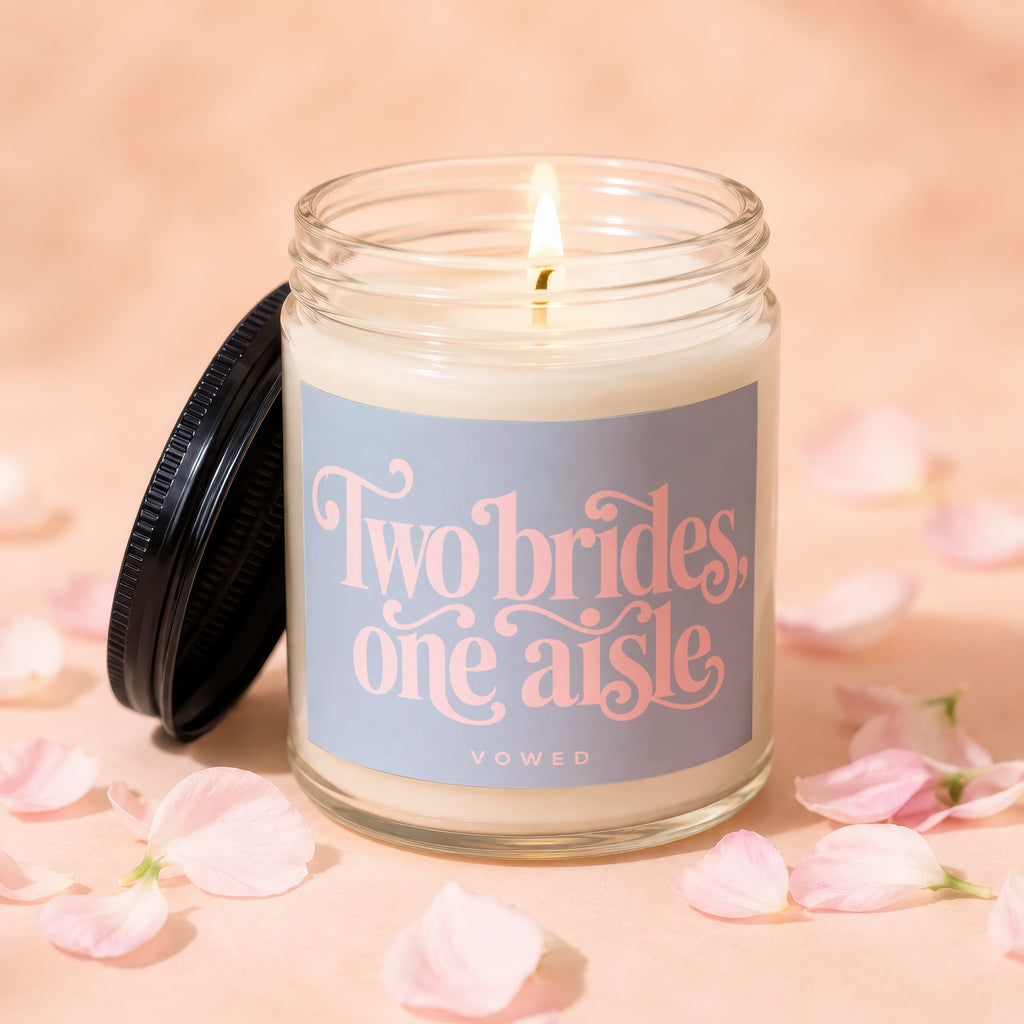 Lit candle with a black lid, labeled "Two brides, one aisle VOWED".