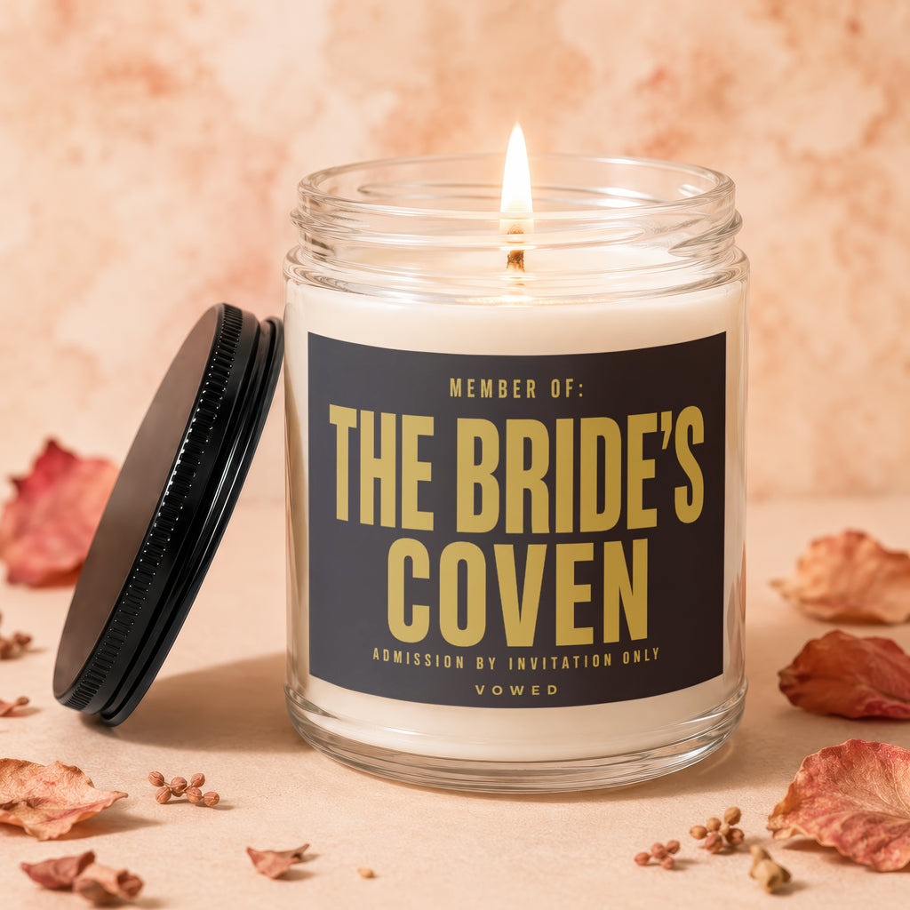 Glass jar candle with lid off, lit wick, and "The Bride's Coven" text.