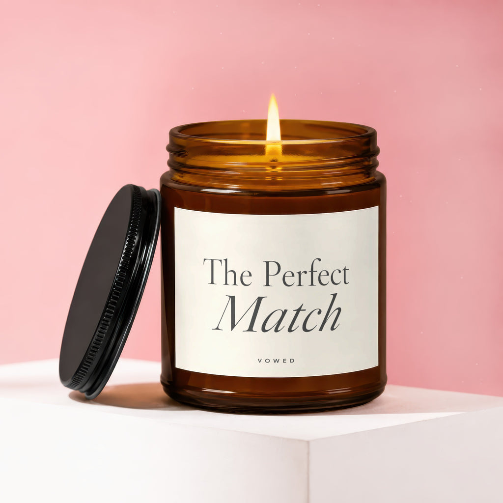 Amber jar candle with lit flame and black lid, labeled "The Perfect Match" and "vowed".