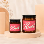 Two amber glass candles with "TYING THE Knot" labels and black lids, displayed on pedestals.