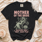 Black t-shirt with "Mother of the Bride Raising Hell Not Just Her" text and skeleton graphic.