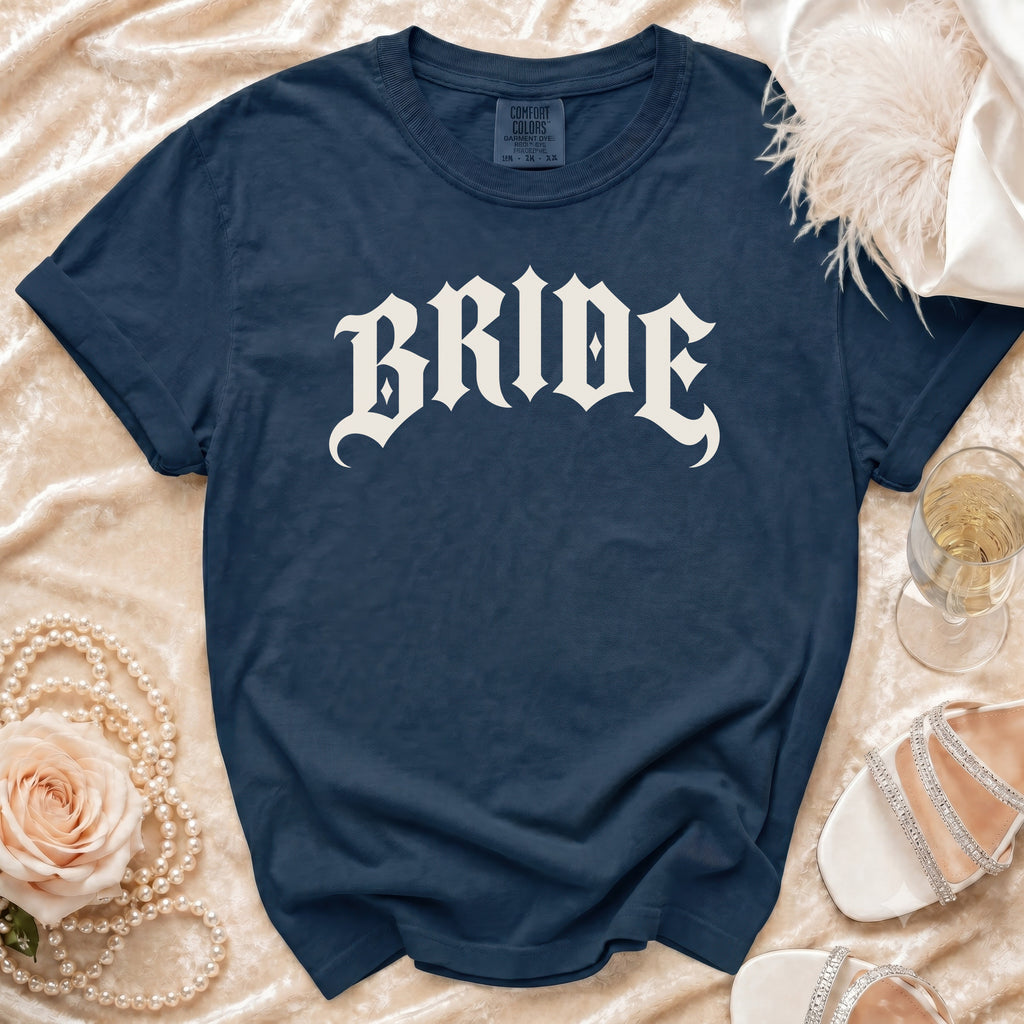 Navy t-shirt with white gothic "BRIDE" text, styled with pearls, rose, and champagne.