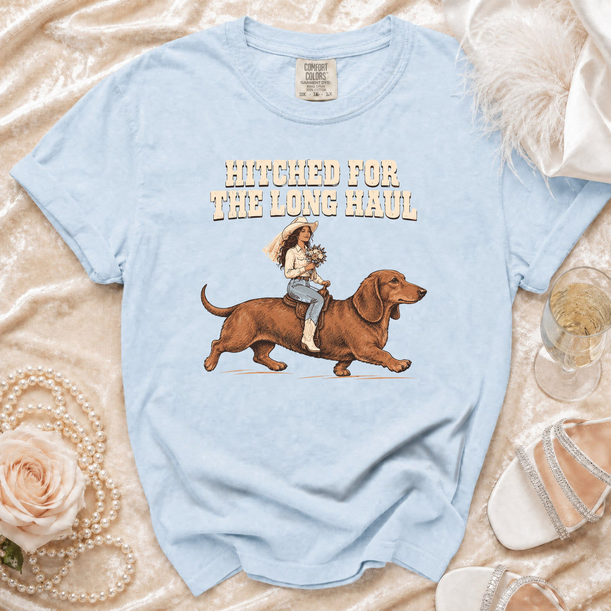 Light blue t-shirt with "Hitched for the Long Haul" graphic of a bride riding a dachshund.