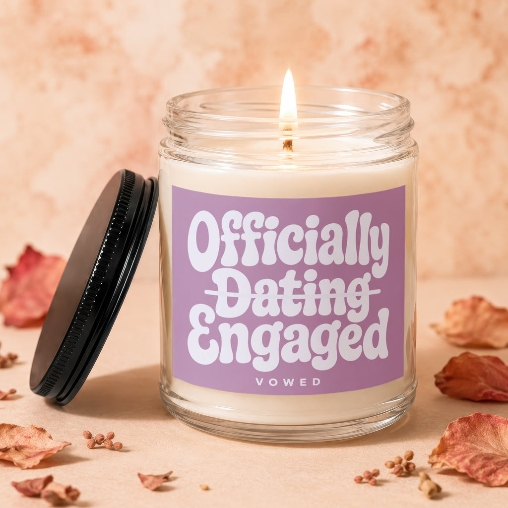 Lit candle in glass jar with purple label reading "Officially Dating Engaged VOWED".