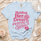 Light blue t-shirt with "Holding Her Dress and Her Secrets" in pink.