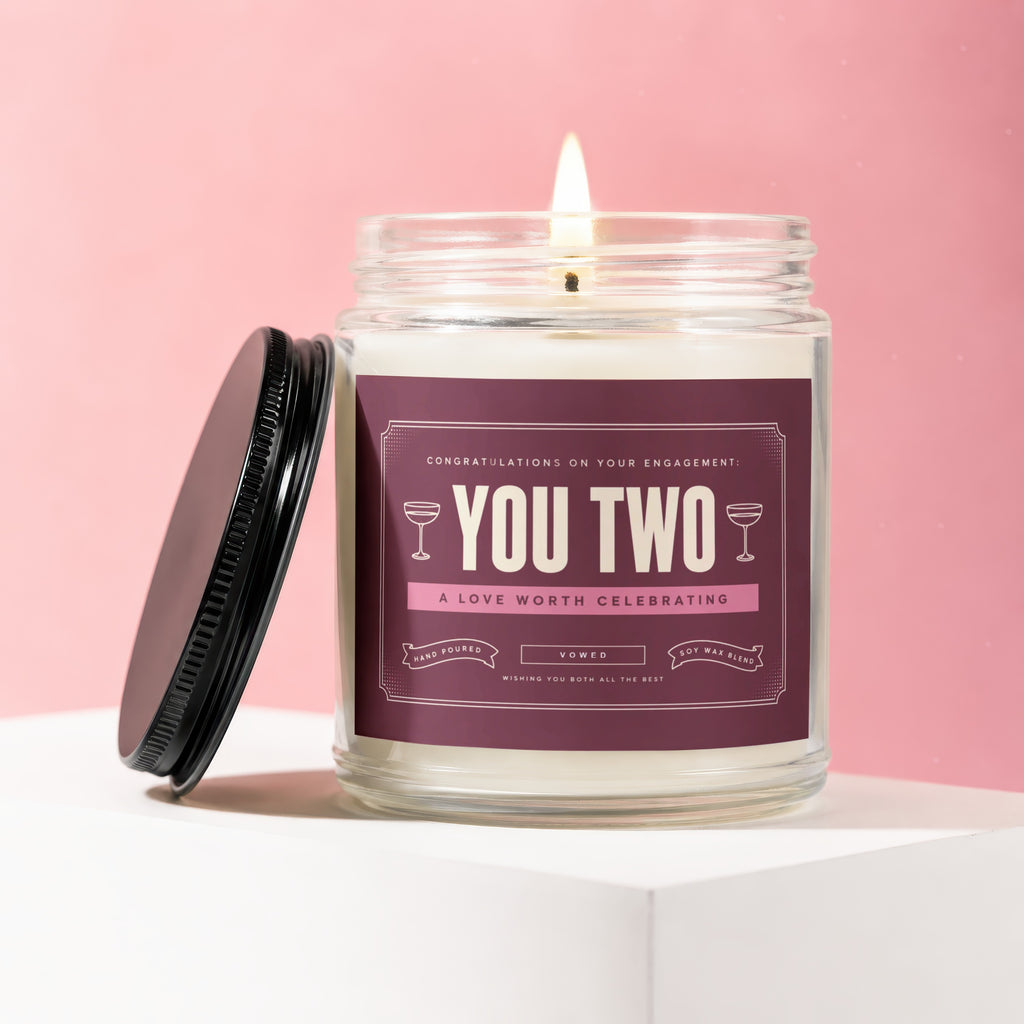 Glass jar candle with a lit wick, reads "You Two" and "Congratulations on your engagement."