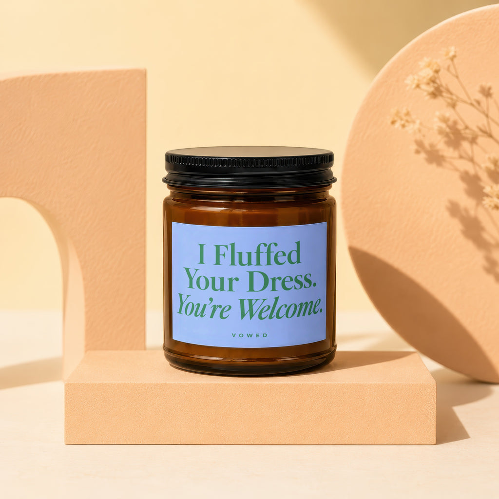 Brown candle with a blue label text "I Fluffed Your Dress. You're Welcome. VOWED."