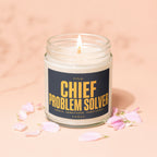 Lit candle in a jar with the label "Chief Problem Solver Vowed Unpaid. Unmatched. Unbothered."