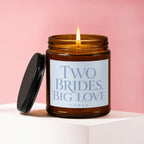 A lit amber glass candle with label reading "Two Brides, Big Love"