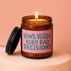 Amber jar candle with lit wick and lid off, reading "Vows, Veils & Very Bad Decisions".