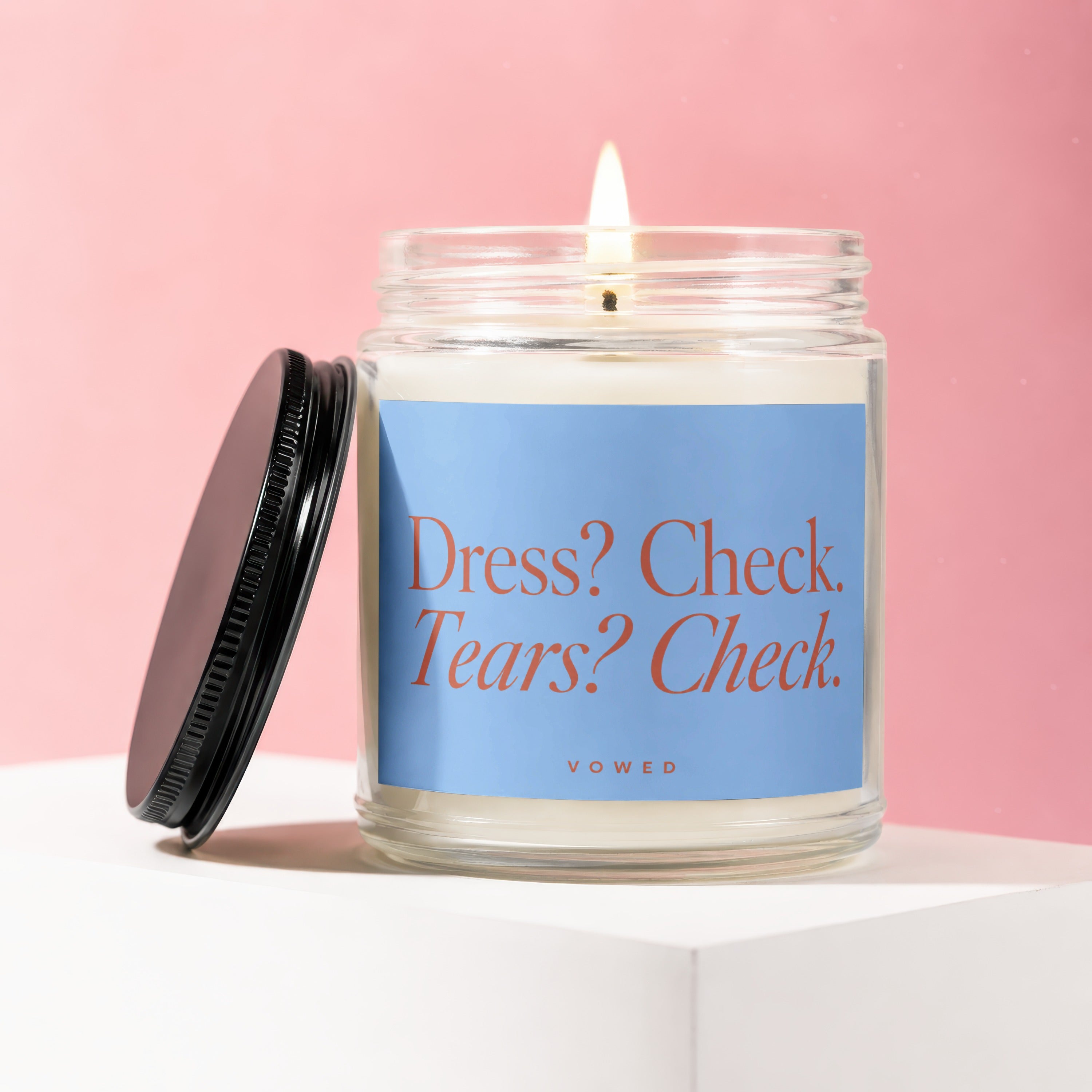 Candle with "Dress? Check. Tears? Check." and "VOWED" text on light blue label.