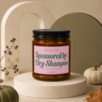 Amber jar candle with "Sponsored by Dry Shampoo" text on pink label.