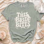 Sage t-shirt with "THIS BRIDE BITES" graphic featuring vampire teeth and wedding elements.