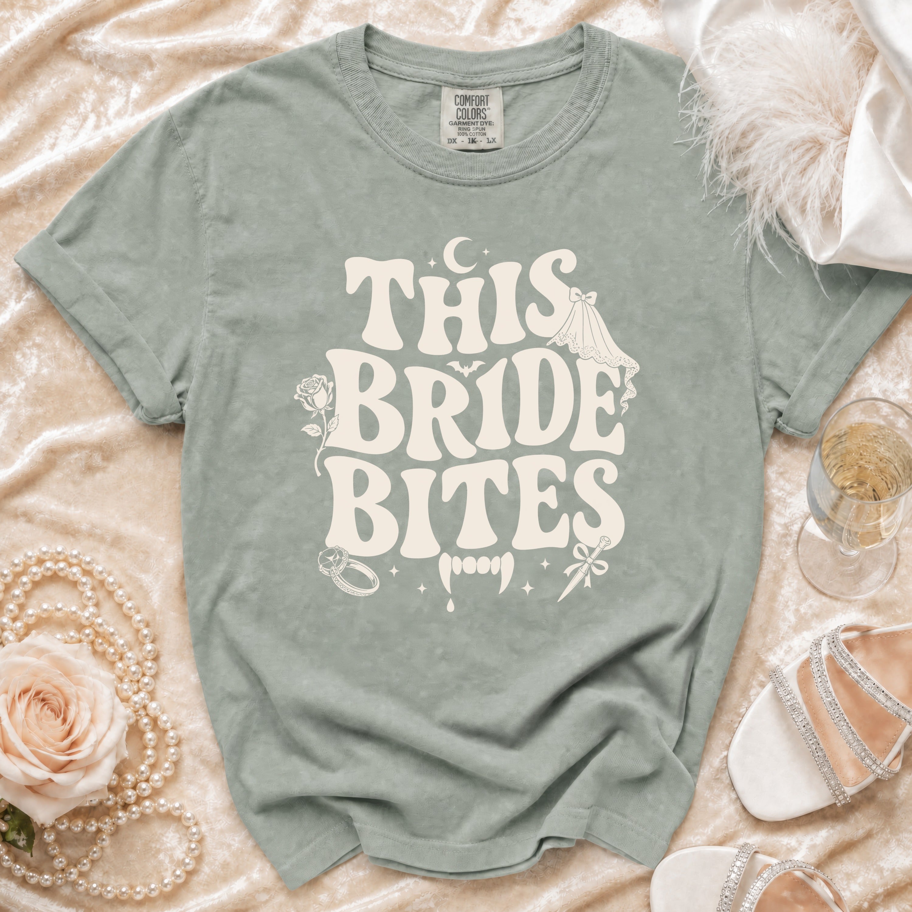 Sage t-shirt with "THIS BRIDE BITES" graphic featuring vampire teeth and wedding elements.
