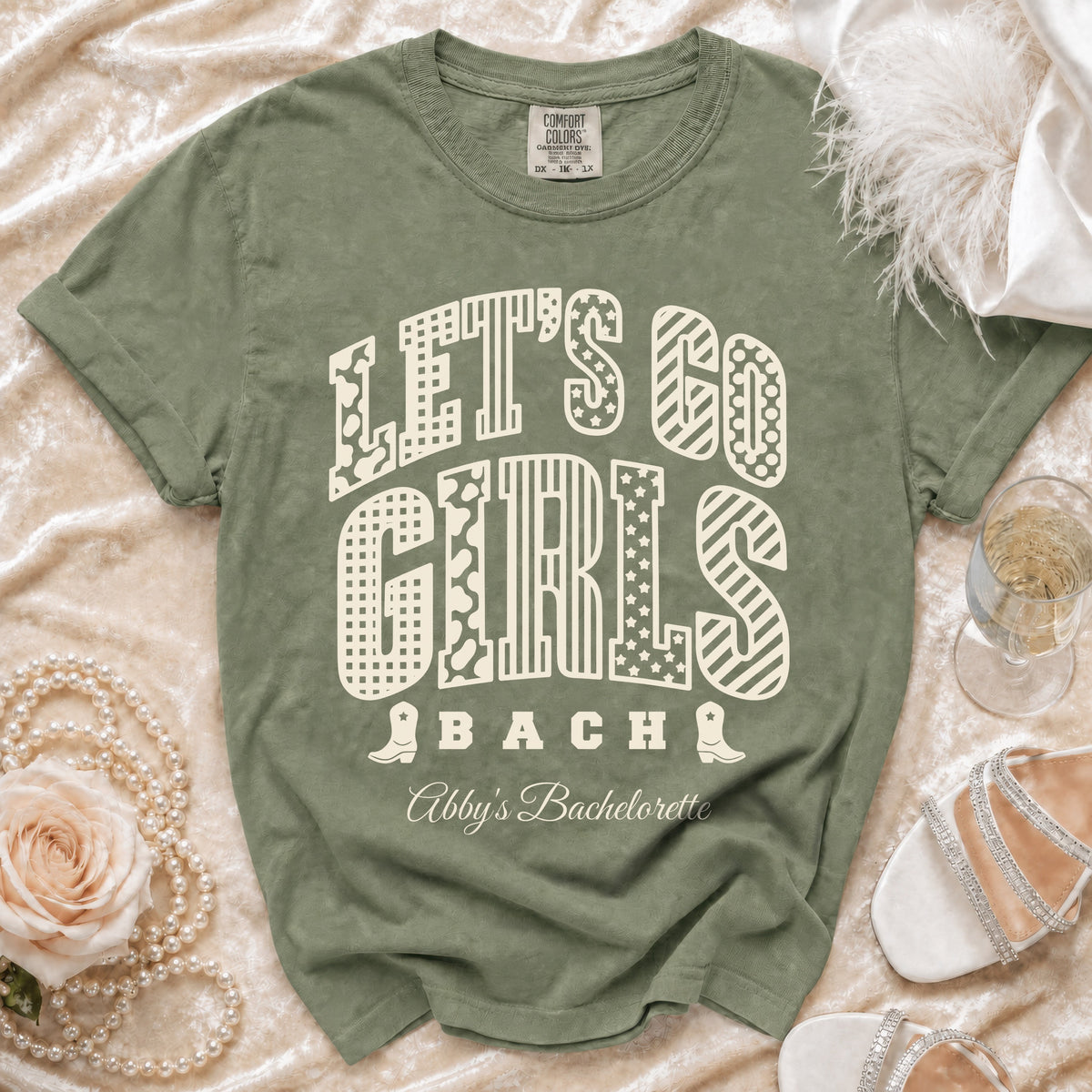 Sage green t-shirt with Let's Go Girls Bach and Abby's Bachelorette text printed in cream.