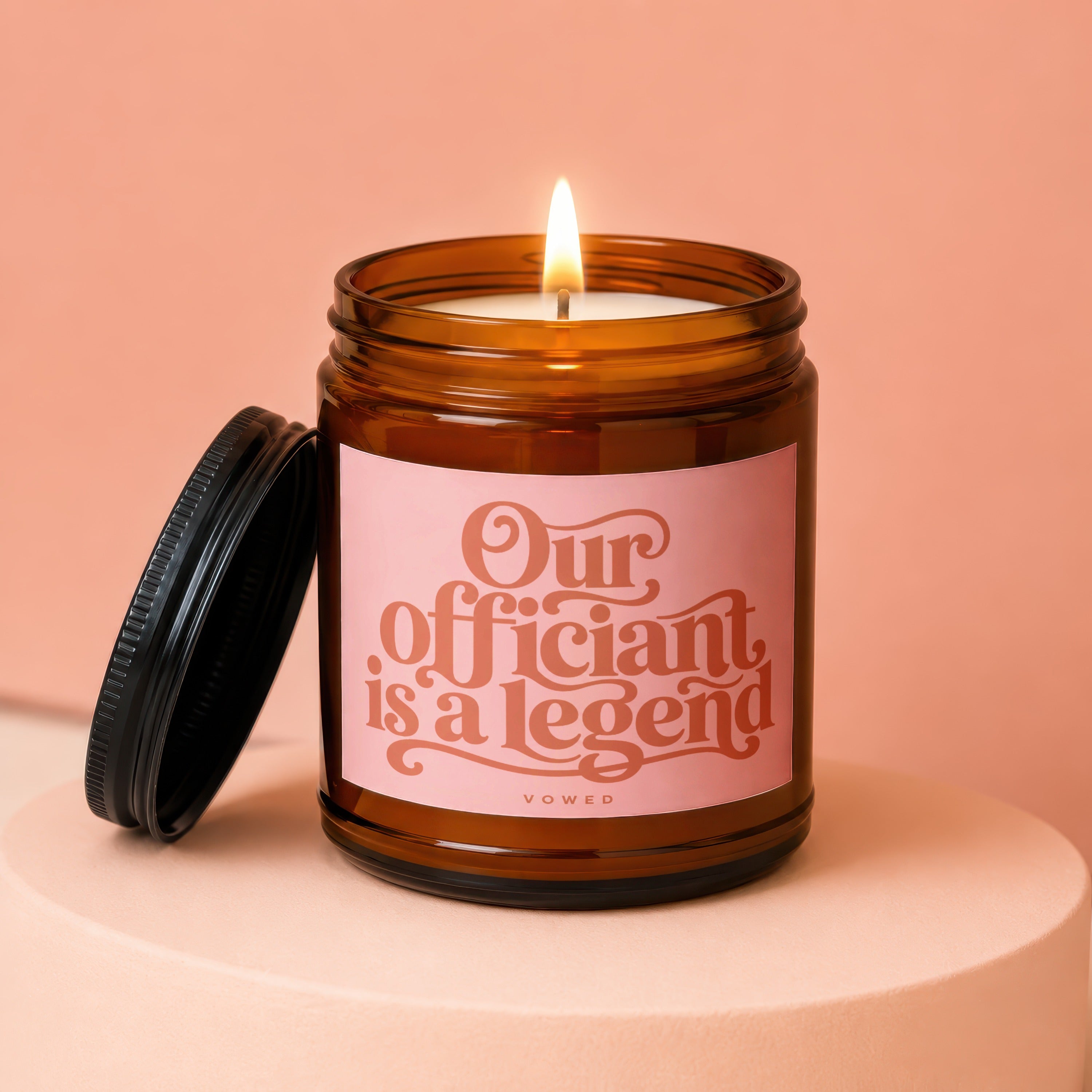 Amber glass candle with pink label reading "Our officiant is a legend".