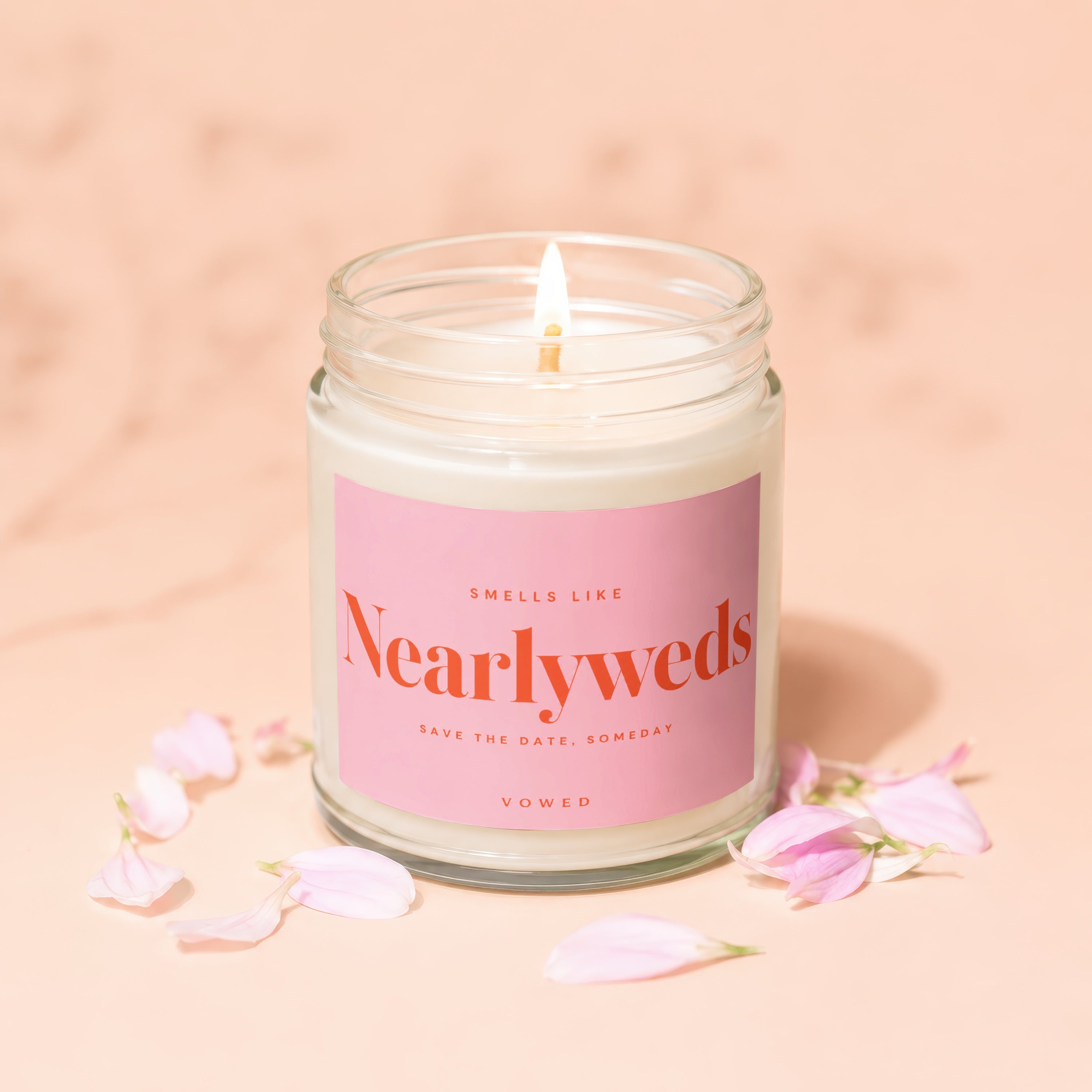 Candle with "Smells Like Nearlyweds" text, lit wick, and pink petals.