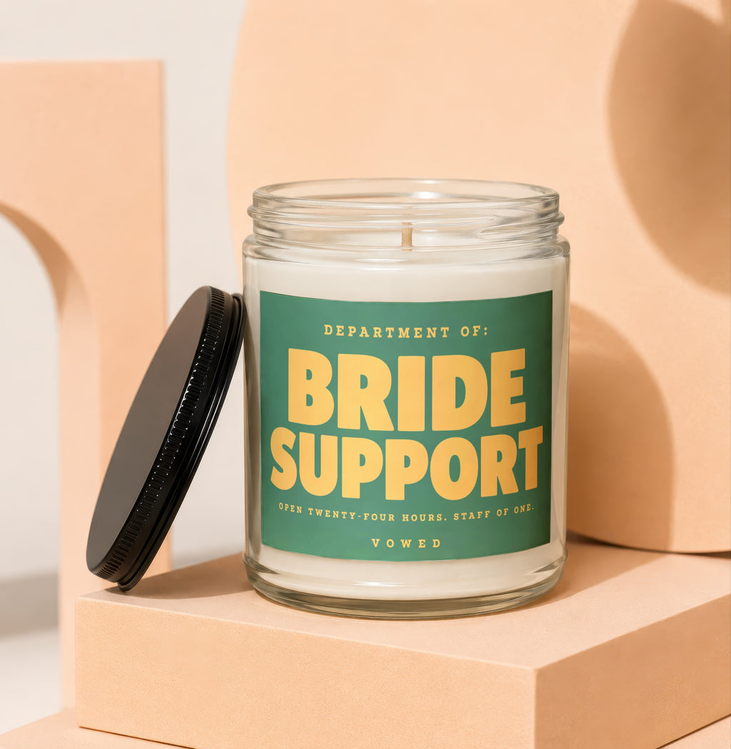 Glass candle with green label reading "BRIDE SUPPORT" and "VOWED".