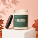 Candle with label "DON'T BLOW IT SHE IS A KEEPER" on white cube.