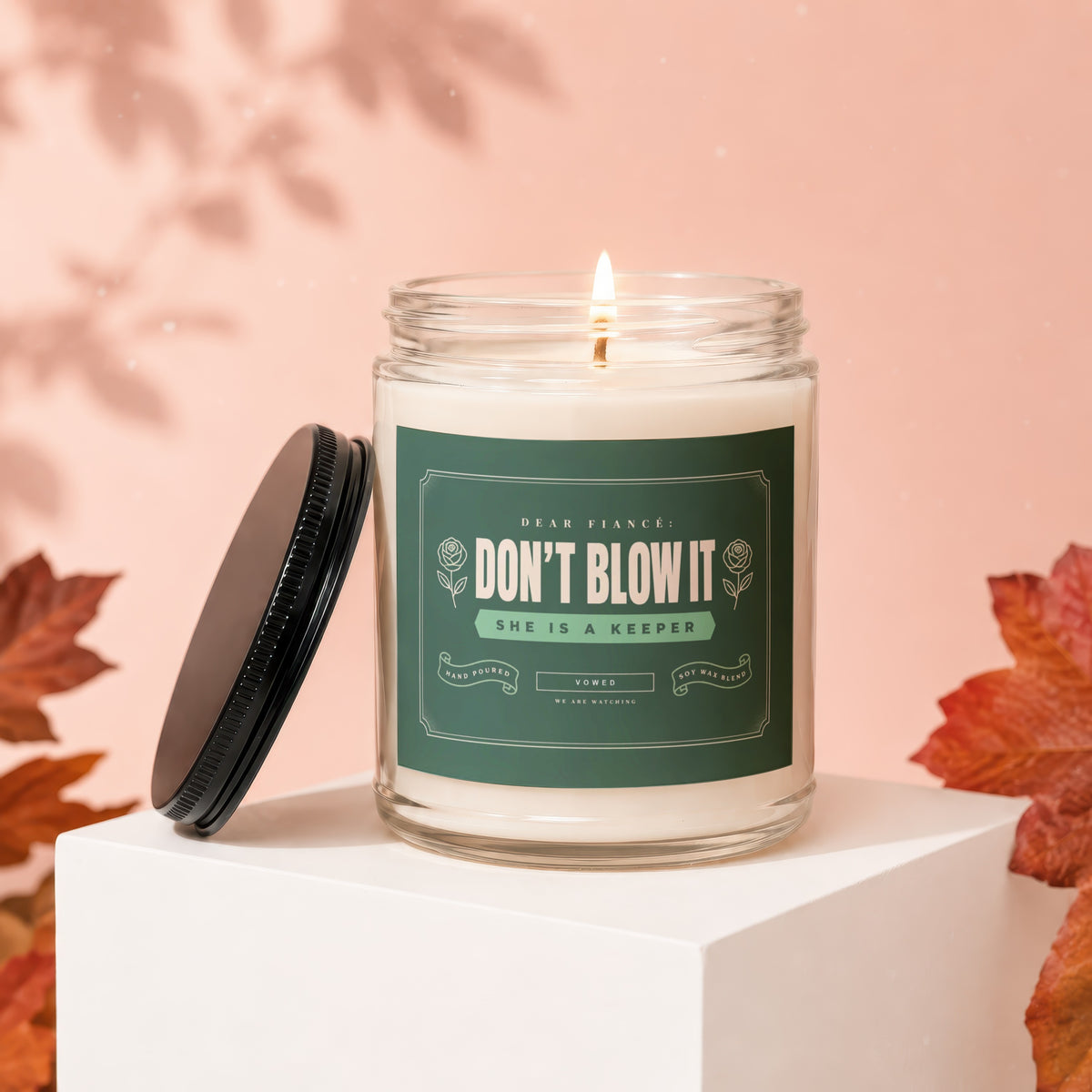 Candle with label "DON'T BLOW IT SHE IS A KEEPER" on white cube.