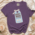 Purple t-shirt with "HONEY MOON in progress" text and champagne glasses graphic.