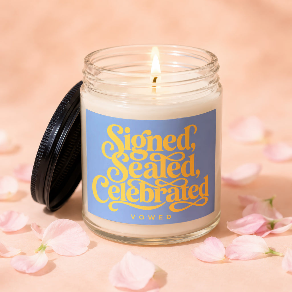 Lit candle in glass jar with blue label reading "Signed, Sealed, Celebrated VOWED"