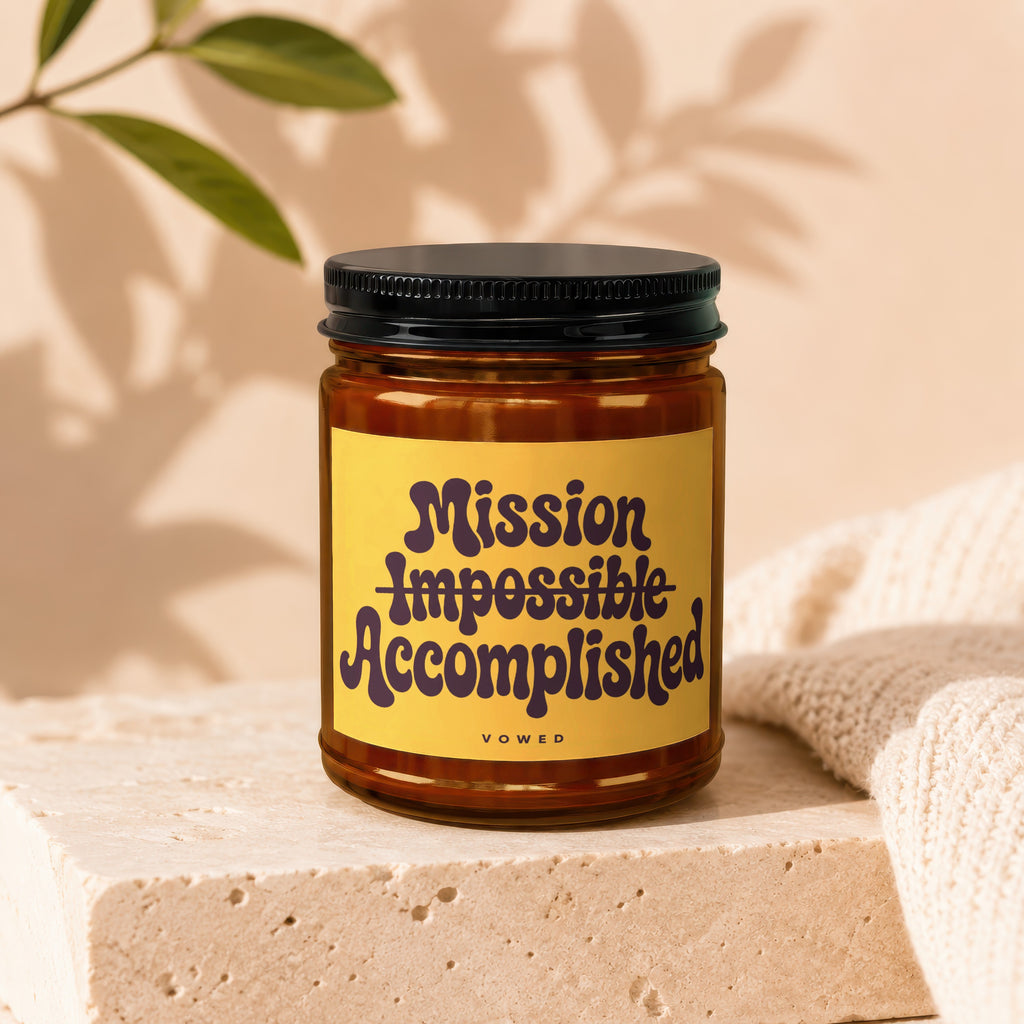 Amber jar candle with yellow label reading "Mission Impossible Accomplished Vowed".