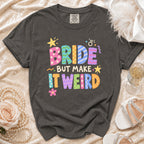 Dark gray t-shirt with "BRIDE BUT MAKE IT WEIRD" text in colorful, patterned letters.