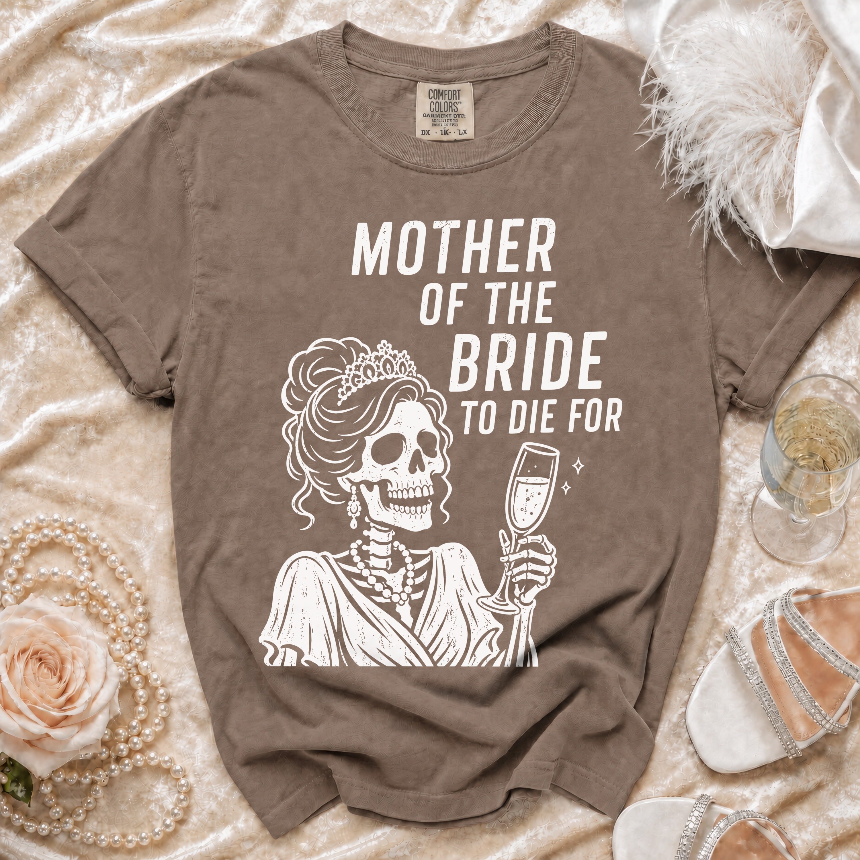 Brown t-shirt with white graphic of a skeleton bride holding champagne and text "Mother of the Bride To Die For".