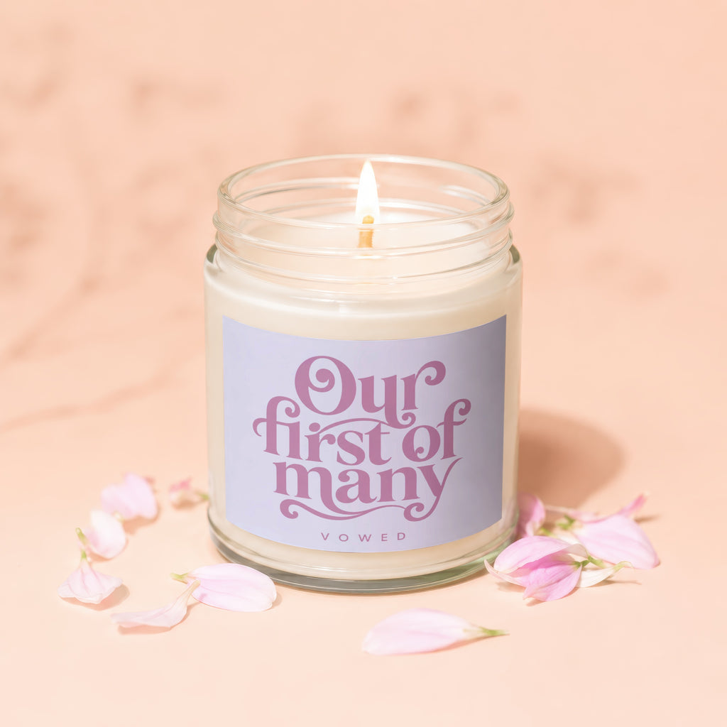 Candle in glass jar with a lit wick, labeled "Our first of many" and "VOWED".