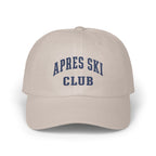 Light beige baseball cap featuring embroidered blue collegiate-style text reading APRES SKI CLUB on the front.