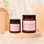 Two amber glass candles with pink labels, one larger, both read "bridesmaid" and a description.