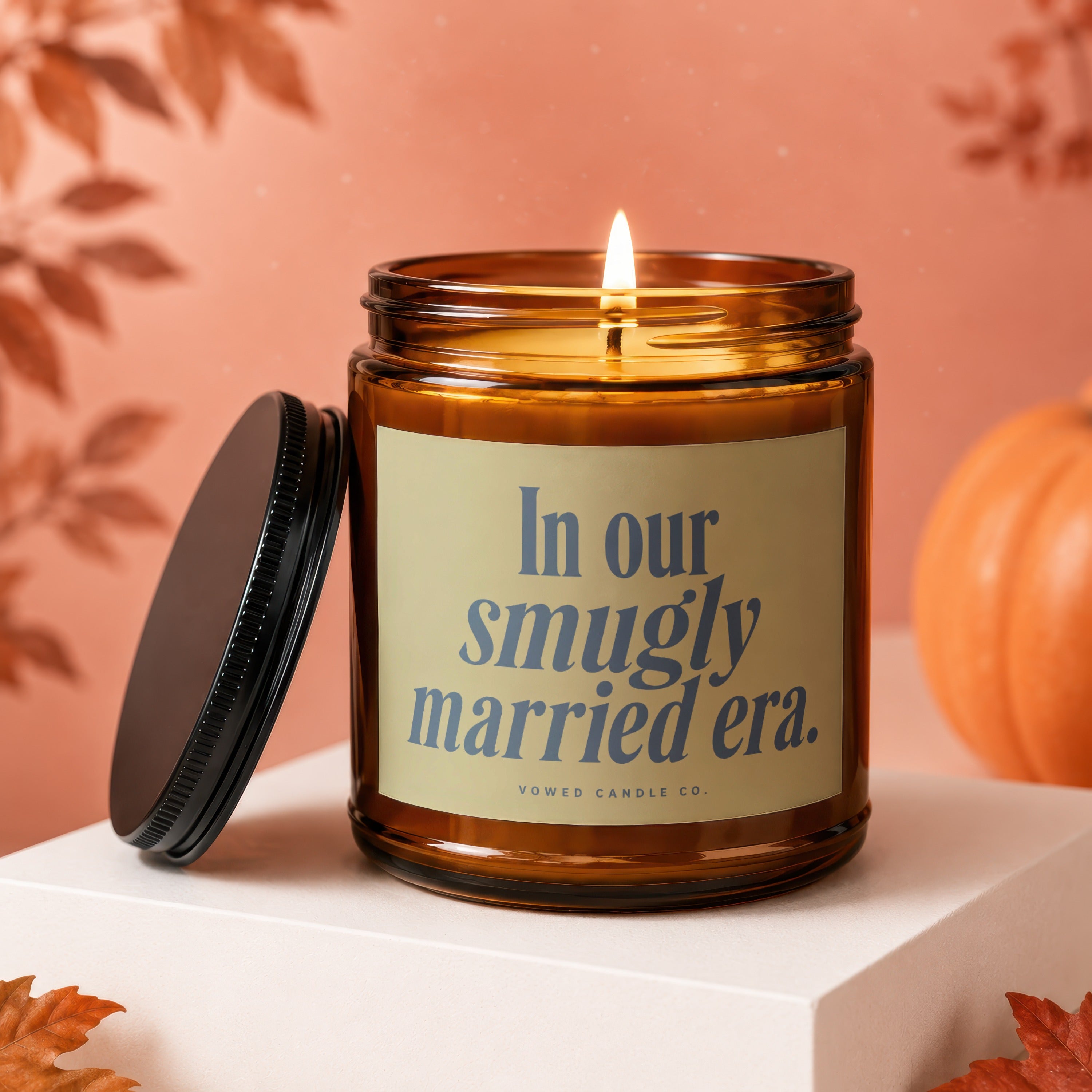 Amber candle with lit wick, lid off, displaying "In our smugly married era." text.