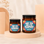 Two amber glass candles with black lids and bold labels saying "Say Yes Or I'm Eloping!"