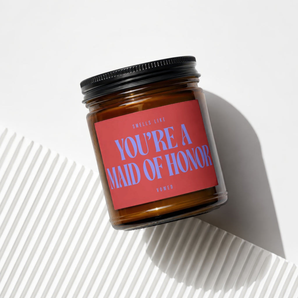 Amber jar candle with red label reading "SMELLS LIKE YOU'RE A MAID OF HONOR"