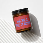 Amber jar candle with red label reading "SMELLS LIKE YOU'RE A MAID OF HONOR"