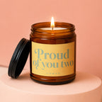 Amber jar candle with lit wick on display pedestal, text "Proud of you two VOWED".