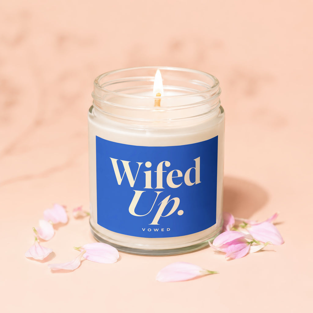Lit candle with "Wifed Up." label surrounded by scattered pink petals.