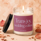 Candle with lit wick and "Trans joy, wedding edition" text on label, topped with lid.