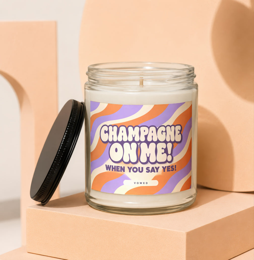Glass candle with "Champagne On Me! When You Say Yes!" text on wavy label.