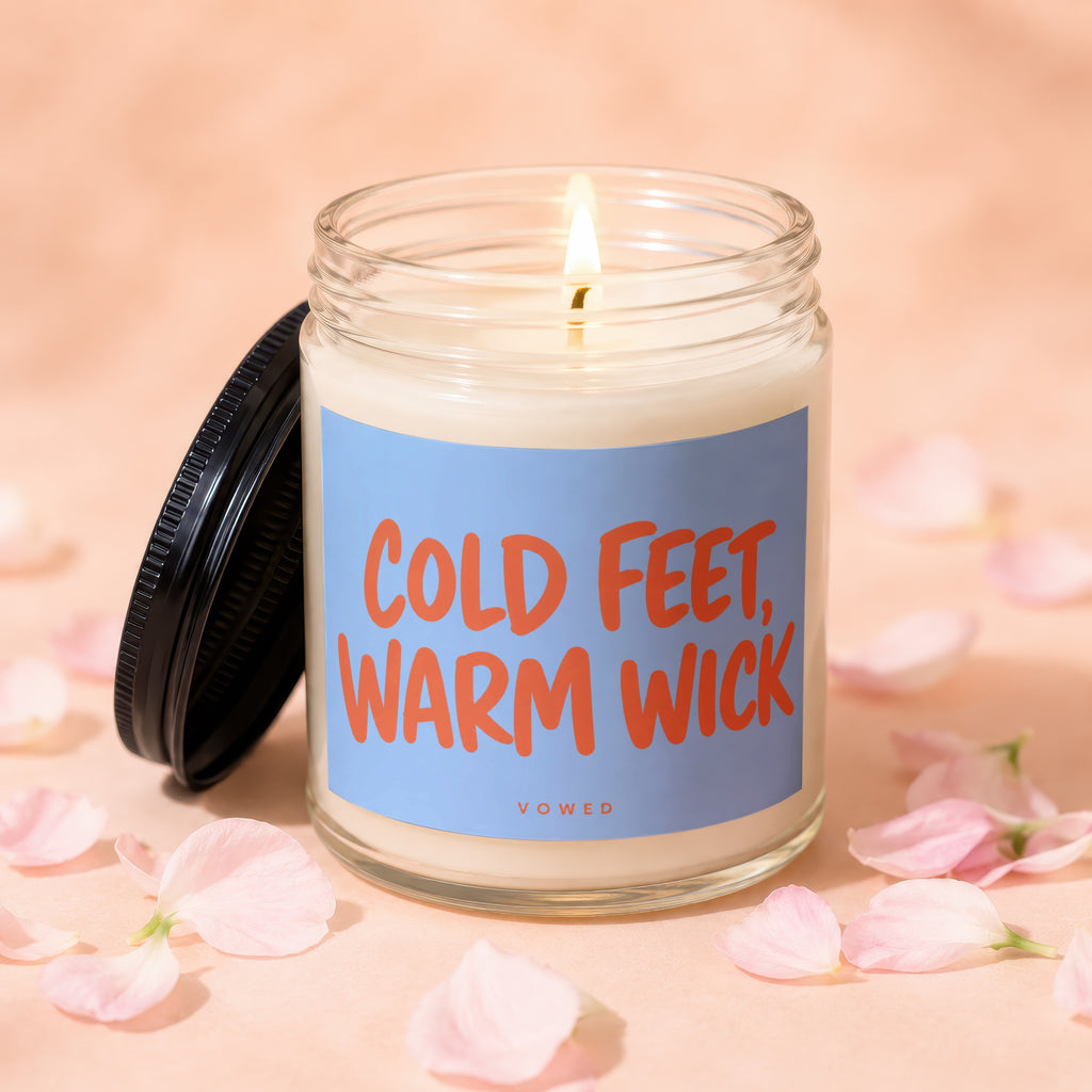 Glass jar candle with "COLD FEET, WARM WICK" on blue label, lid ajar.