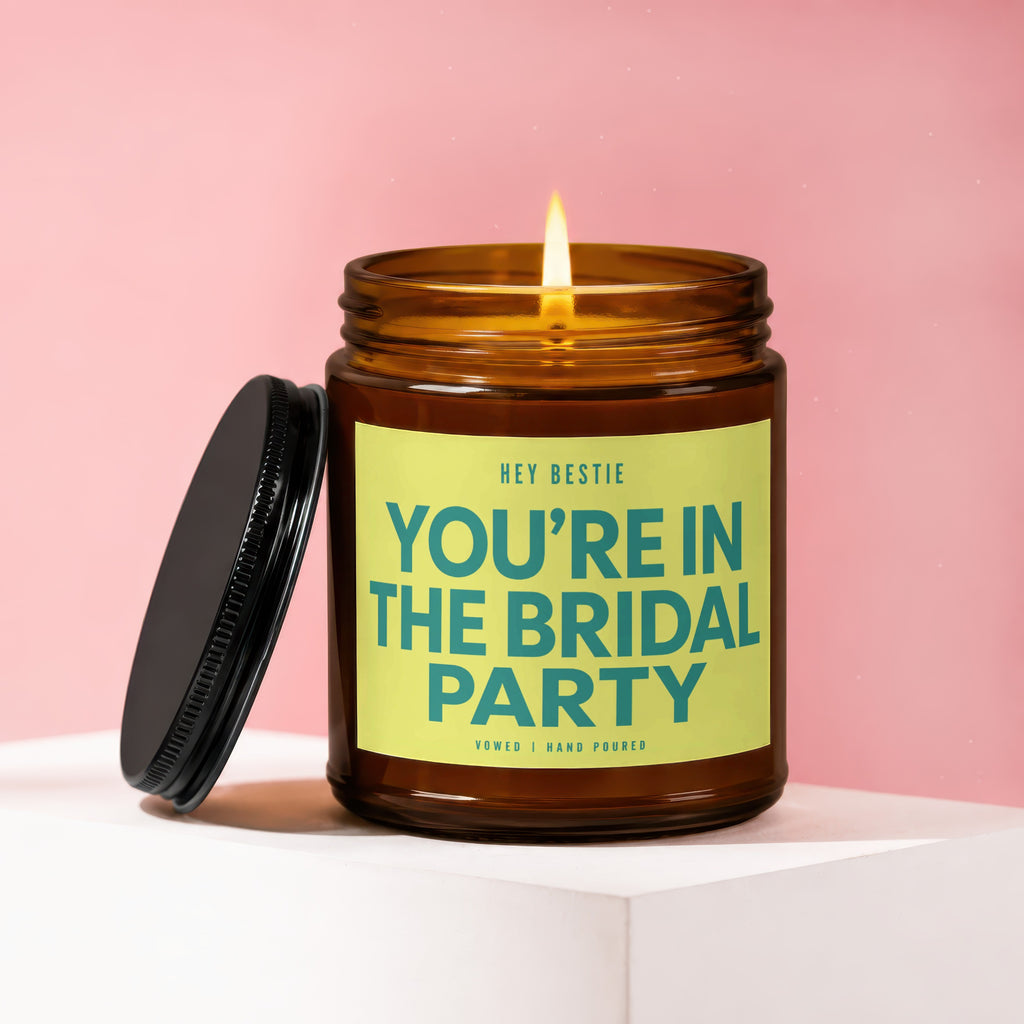 Amber jar candle with lit flame and lid off, reads "YOU'RE IN THE BRIDAL PARTY".